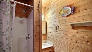 A wooden cabin bathroom with a shower, sink, and decorative fish-themed mirror. - Get hooked on "The Fish House"! (HATTERAS)