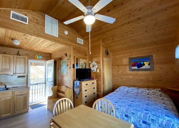 A wooden cabin interior with a kitchen, dining area, and a bedroom.
