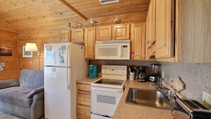A compact kitchen with wooden cabinets, a refrigerator, a microwave, a stove, a sink, and a toaster. - Get hooked on "The Fish House"! (HATTERAS)