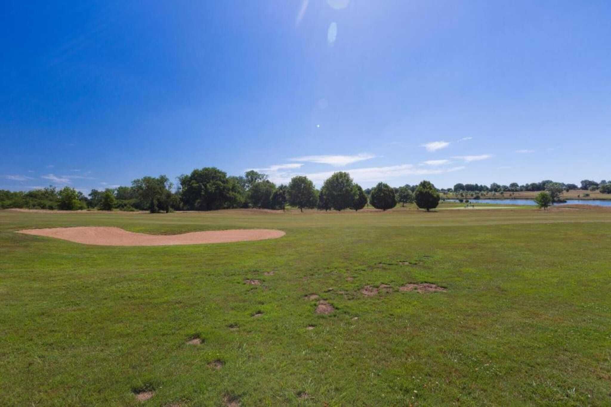 A large open grassy field with a baseball diamond and trees in the background.