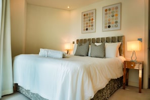 A neatly made bed with white linens, two wall-mounted lamps, and a framed artwork above the bed. - A luxurious apartment, fully equipped. (PORTSMOUTH)