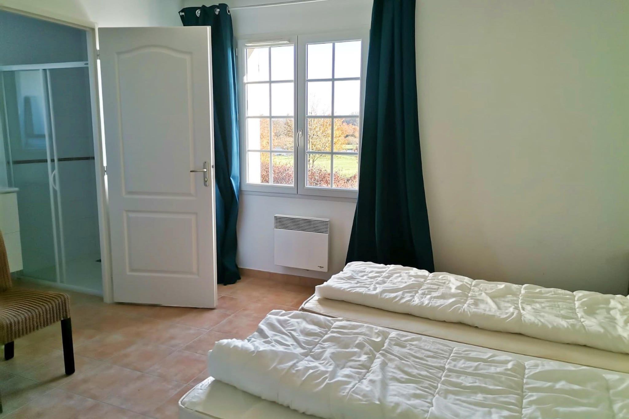 A room with a bed, a chair, a radiator, and a window with curtains.