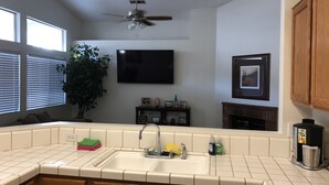 Una cocina con una isla grande, un lavamanos, gabinetes de madera, un ventilador de techo, un televisor de pantalla plana y una chimenea.