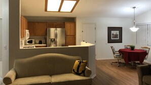Una sala de estar con sofá, un comedor con mesa y sillas, una cocina con armarios de madera y electrodomésticos, y un candelabro en el techo.
