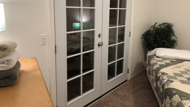 Un dormitorio con puerta doble, una cama con cubrecama floral, una planta en la mesita de noche y una lámpara.