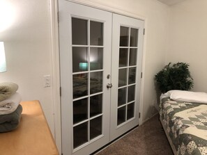 A bedroom with a double door, a bed with a floral bedspread, a bedside plant, and a lamp on a nightstand. - Contemporary Zen Getaway with Two-Car Garage (Bakersfield)
