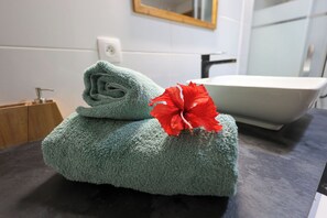Un baño con lavamanos, espejo y toalla con estampado de hibisco.