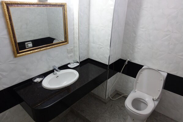 A bathroom with a black countertop, white sink, and a toilet. - Serene Hotel (Pattaya)