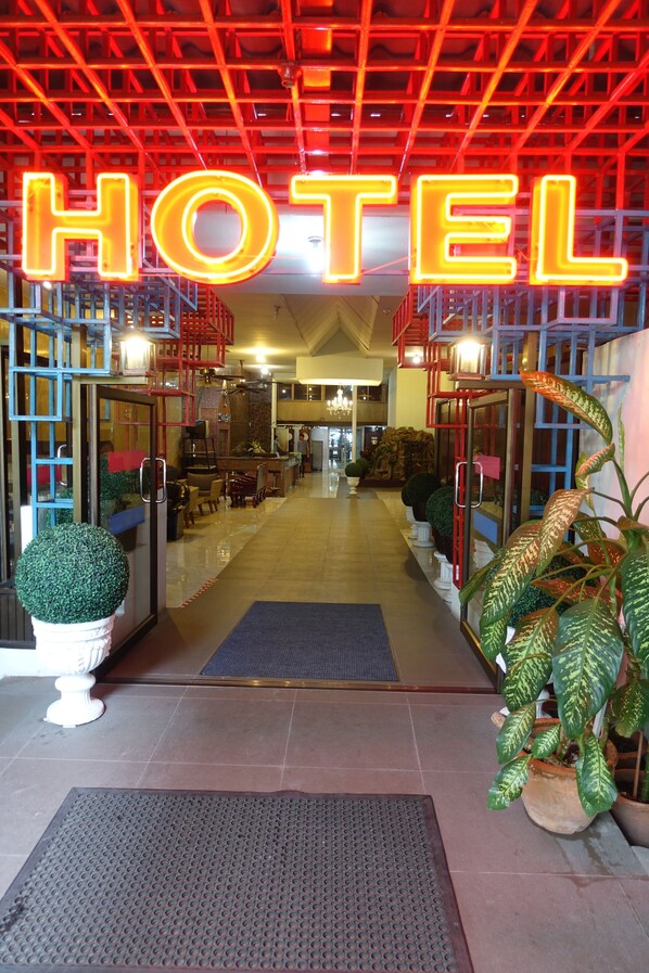 A hotel entrance with a neon 'HOTEL' sign, a reception desk, and potted plants. - Serene Hotel (Pattaya)