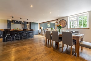A modern kitchen with wooden flooring, a dining area with a wooden table and chairs, and a large window with a view of greenery.