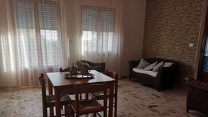 A dining area with a wooden table and chairs, a woven sofa, and a stone-patterned floor. - Trilocale 150mt from the sea of La Caletta of Siniscola Nuoro Sardinia Italy (La Caletta)
