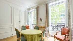 A dining room with a round table, green upholstered chairs, and a red upholstered chair. - By Boulevard Saint Germain, by Veeve (Paris)