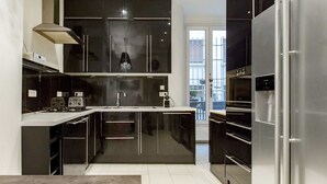 A modern kitchen with black cabinets, stainless steel appliances, and a central island. - By Boulevard Saint Germain, by Veeve (Paris)