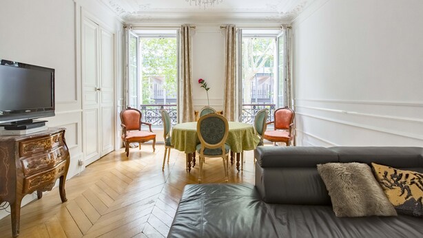 A living room with a television, a sofa, a dining table with chairs, and a balcony with a railing. - By Boulevard Saint Germain, by Veeve (Paris)