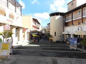 A street view with a building featuring a sign for 'EXPRESS' and another for 'VENTES'. There are potted plants along the sidewalk and a signboard with text. - Cap-Esterel Village Studio 4 people Air-conditioned Selection (Agay)