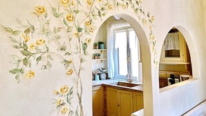 A kitchen with wooden cabinets, a window with a curtain, and a floral wall mural. - Beautiful View in a Shabby Chic Atmosphere (Padenghe Sul Garda)