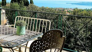 A terrace with a table and chairs, overlooking a coastal landscape with trees and a view of the sea. - Beautiful View in a Shabby Chic Atmosphere (Padenghe Sul Garda)