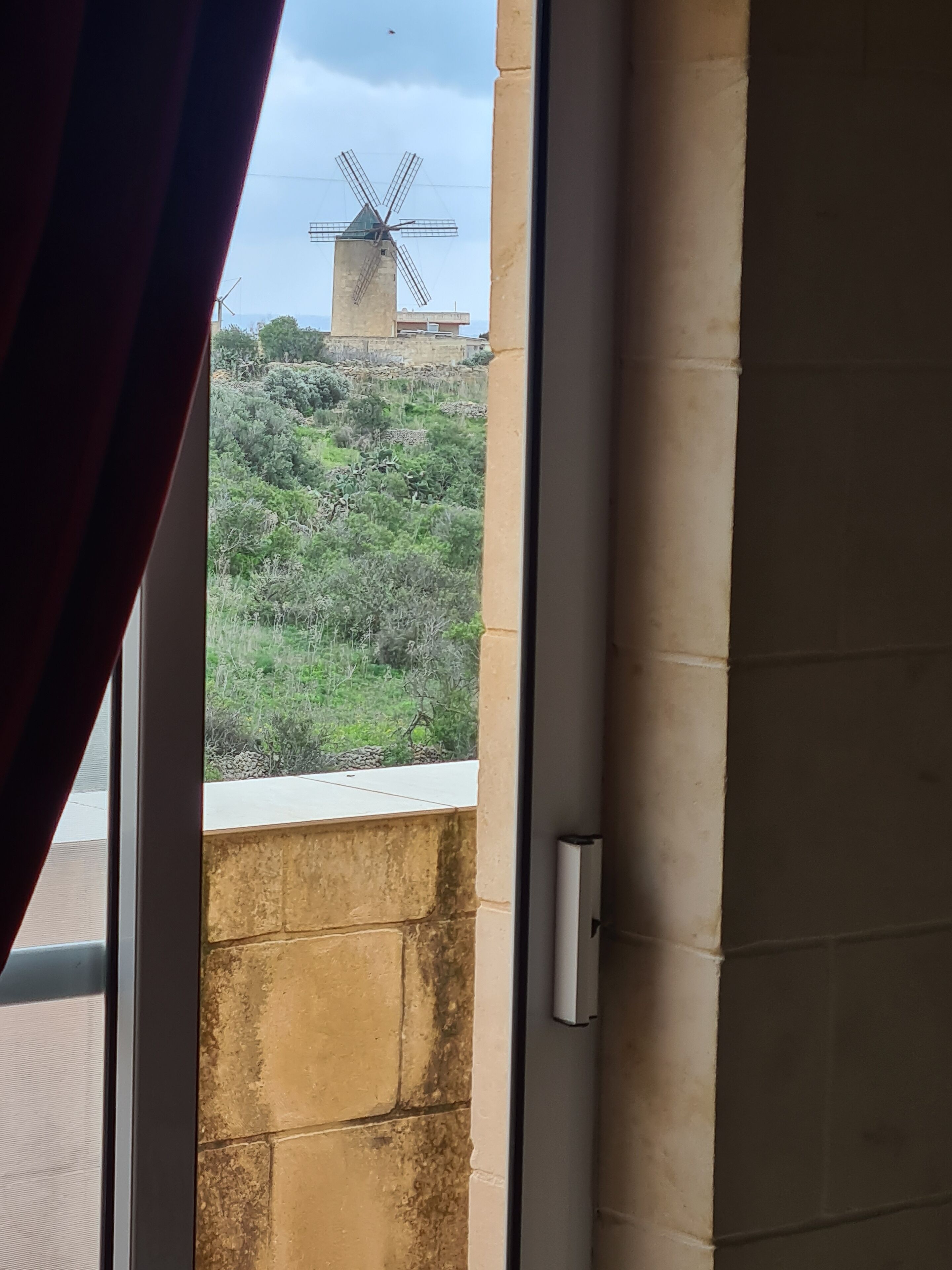 A window view of a windmill, a stone wall, and a door frame.
