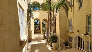 A narrow corridor with a tiled floor, white railings, and potted plants. - IL-BEJTA  PENTHOUSE. (Il-Qala)