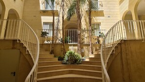 A multi-level interior with a central staircase, balconies with railings, and potted plants. - IL-BEJTA  PENTHOUSE. (Il-Qala)