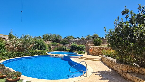 A swimming pool with a stone wall and potted plants around it. - IL-BEJTA  PENTHOUSE. (Il-Qala)