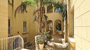 A narrow corridor with a staircase, arched windows, and potted plants. - IL-BEJTA  PENTHOUSE. (Il-Qala)