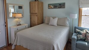 Un dormitori amb llit, una tauleta de nit, un aparador, un ventilador de sostre, una finestra amb cortines i una obra d'art penjada a la paret.