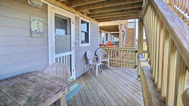 A wooden deck with a covered area, a bench, and two chairs. - Escape to the beach with Cabana By The Sea! (HATTERAS)