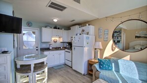 A compact kitchen with white cabinets, a refrigerator, a microwave, and a small dining area with a glass table and two stools. - Escape to the beach with Cabana By The Sea! (HATTERAS)