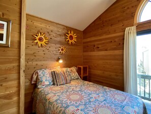 Um quarto de madeira com uma cama, roupa de cama estampada e três decorações em formato de sol.