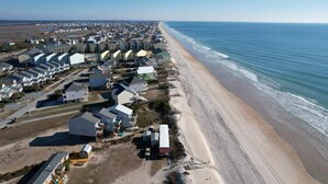 Vue aérienne d’une zone résidentielle côtière, avec des maisons le long de la plage, un ciel dégagé et une mer calme.