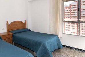 A bedroom with a wooden bed, a nightstand, and a window with a view of a building. - MONTEMAR, C-12º-33 (Cullera)