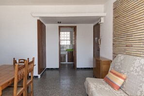 A room with a wooden dining table and chairs, a sofa with a patterned cushion, and a window with blinds. - MONTEMAR, C-12º-33 (Cullera)