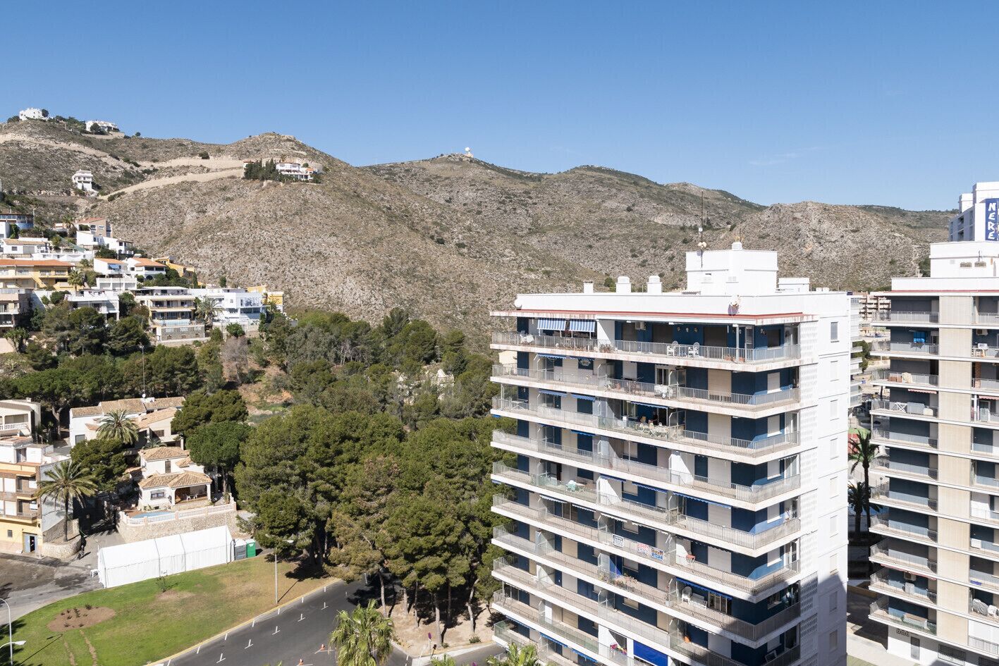 A multi-story hotel with balconies, situated in a hilly area with sparse vegetation.