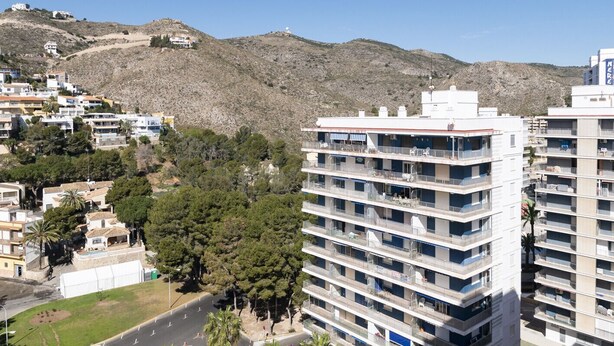 Un hôtel à plusieurs étages, doté de balcons, situé dans une zone vallonnée où la végétation est clairsemée.