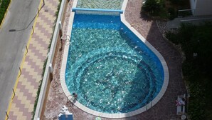 Une piscine à la forme originale, entourée d’une allée pavée en pierre et recouverte de carreaux.