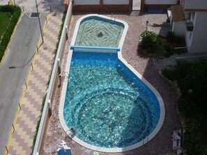 Une piscine à la forme originale, entourée d’une allée pavée en pierre et recouverte de carreaux.