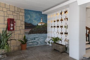 A lobby with a mural of a coastal scene, a fire extinguisher, potted plants, and a white decorative wall. - MONTEMAR, C-12º-33 (Cullera)
