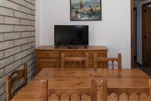 A dining area with a wooden table and chairs, a television on a wooden cabinet, and a painting on the wall. - MONTEMAR, C-12º-33 (Cullera)