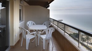 Un balcon avec une table et des chaises, donnant sur une plage et l’océan.
