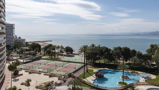 Un resort con cancha de tenis, piscina y vista a la playa.