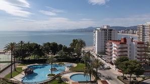 Un resort con una gran piscina, palmeras y vistas al mar y a las montañas.