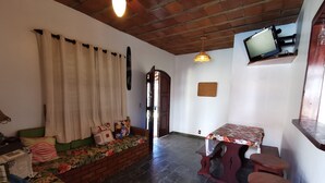 A cozy living area with a sofa, a small table, and a television mounted on the wall. - Beautiful 5 Bedrooms (4 Suites) Air conditioning, swimming pool, barbecue - Saquarema (Saquarema)