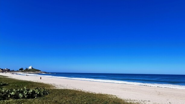 A beach with a white sandy shore, a clear blue sky, and a small white building on a hill. - Beautiful 5 Bedrooms (4 Suites) Air conditioning, swimming pool, barbecue - Saquarema (Saquarema)