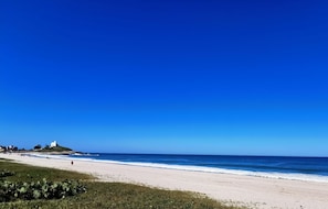 A beach with a white sandy shore, a clear blue sky, and a small white building on a hill.