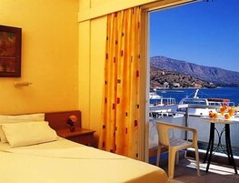 A hotel room with a bed, a small table with a chair, and a view of the sea and boats.