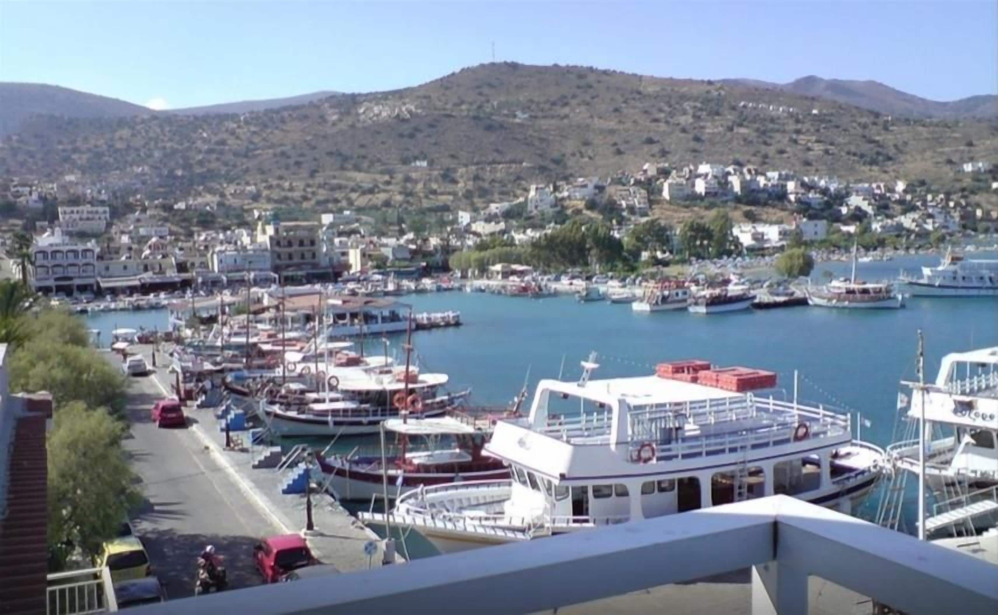 A marina with boats docked, a road with vehicles, and buildings in the background.