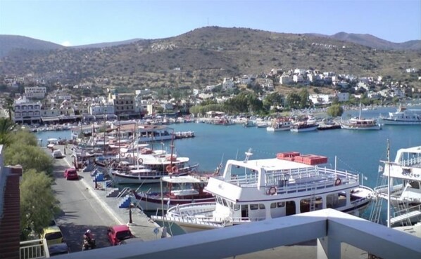 Un puerto deportivo con barcos amarrados, una carretera con vehículos y edificios al fondo.