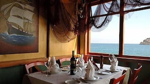 A table set for dining with a view of the sea and a painting on the wall. - Aristea Hotel (Agios Nikolaos)