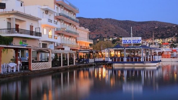A waterfront hotel with multiple balconies and a restaurant named "The Floating Restaurant" docked at the pier. - Aristea Hotel (Agios Nikolaos)